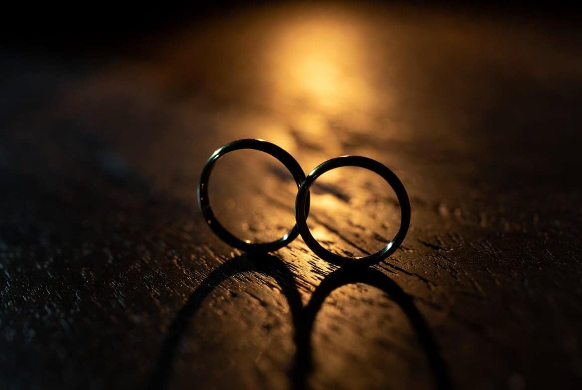 Deux alliances dorées séparées sur table en bois sombre, symbole de la rupture qui menace un couple sous l'effet d'un sihr de séparation actif