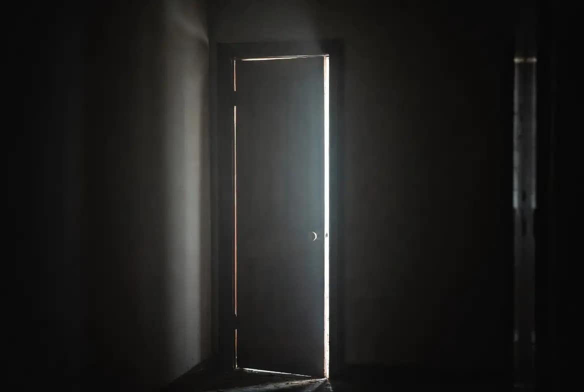 Porte entrouverte dans une maison sombre la nuit, évoquant une présence qui se manifeste par des ouvertures inexpliquées